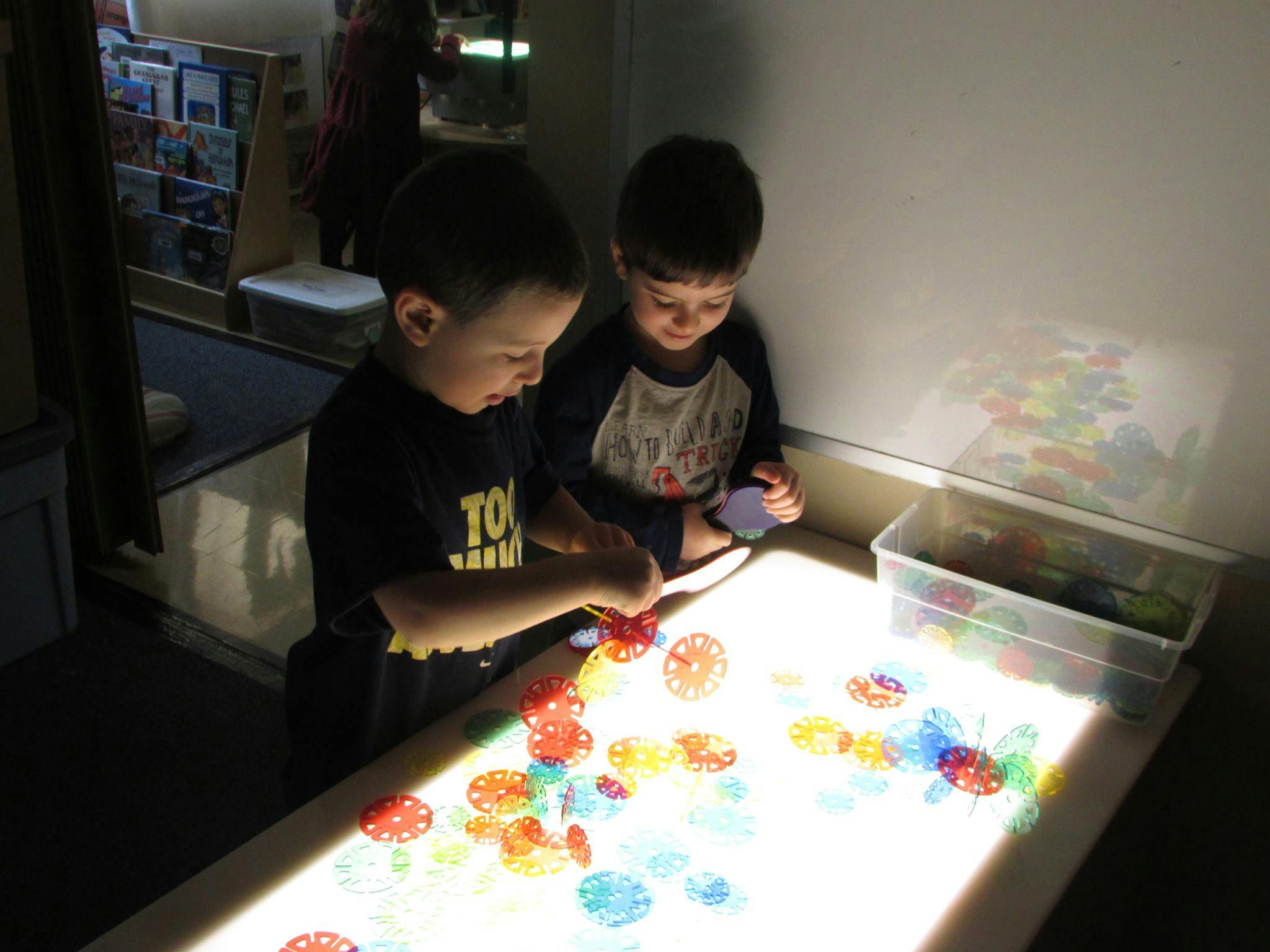 Two children playing with colorful translucent shapes on a light table