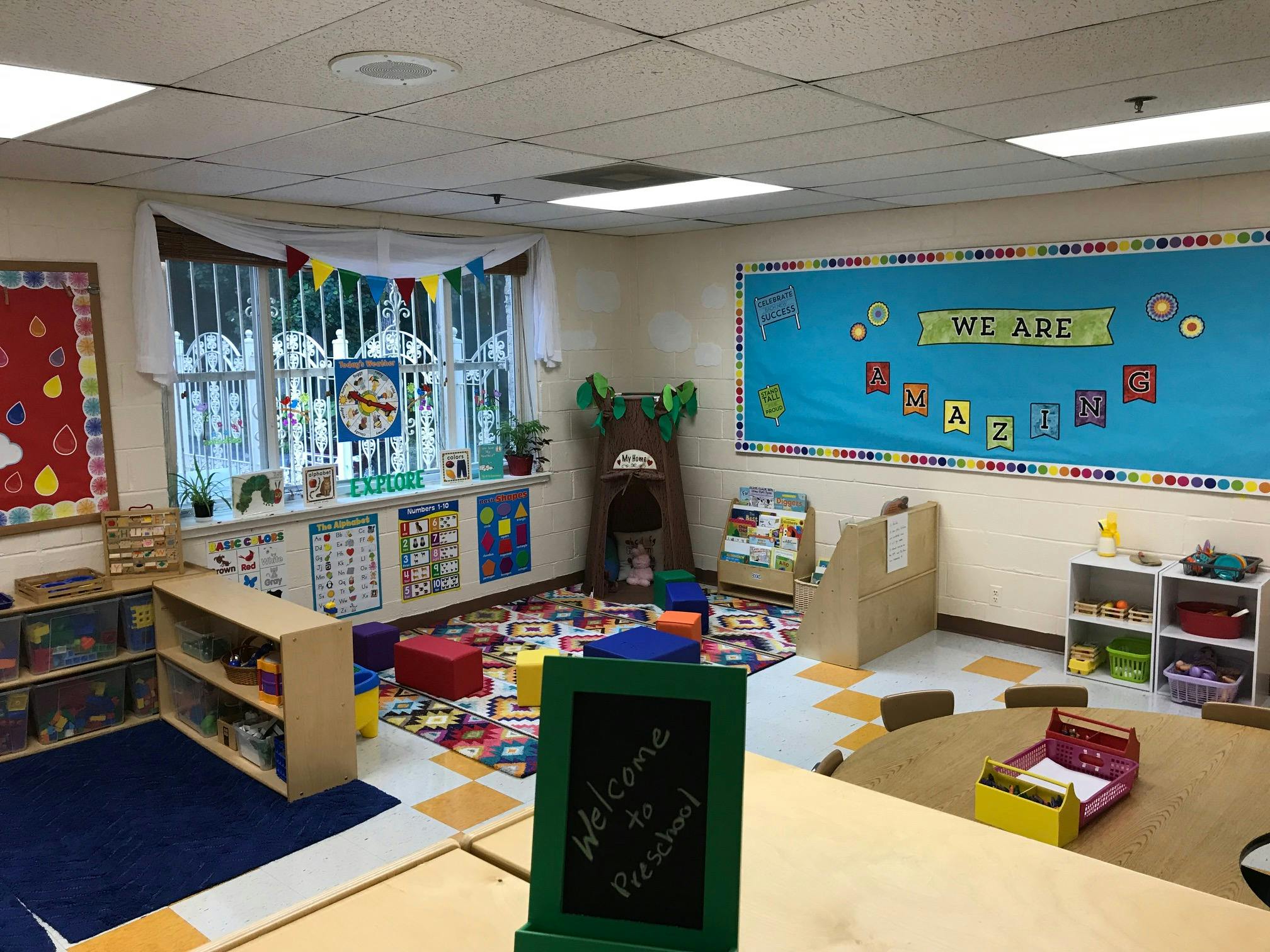 Empty classroom with colorful rug, small tables, and bulletin boards