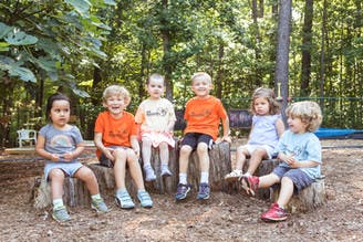 Six children sitting on tree stumps outdoors