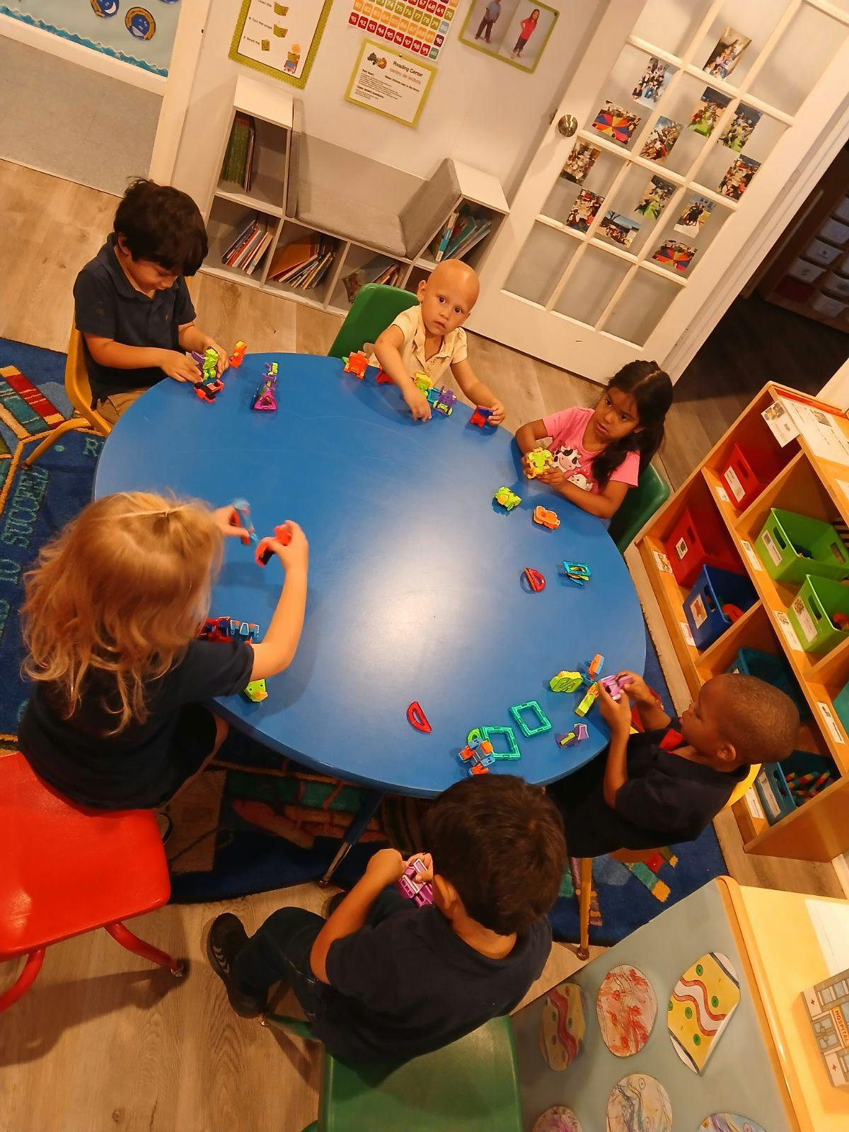 Children playing with toys at a blue table in a classroom