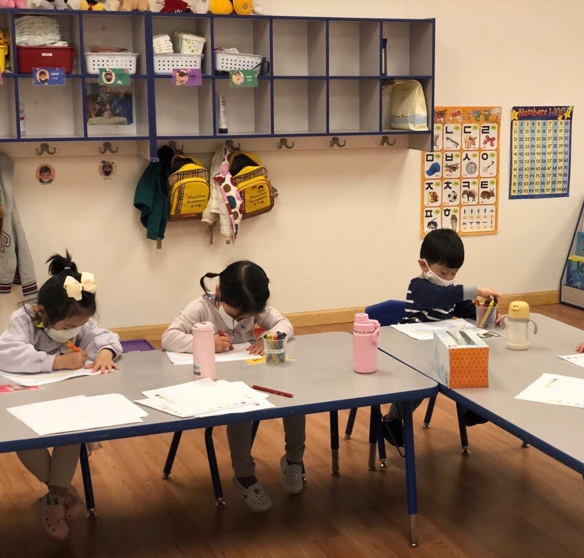 Three children drawing at tables in a classroom