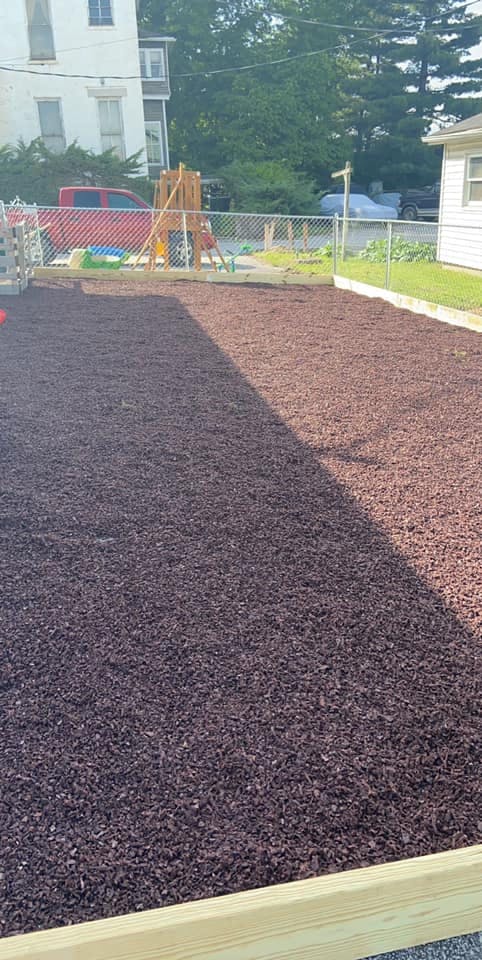Mulched area with a wooden border, chain link fence, and playground in background
