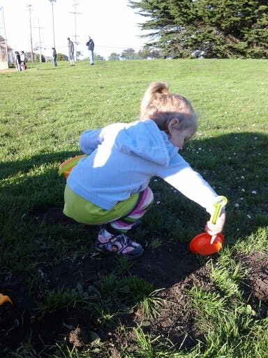 Child crouching and digging in dirt with a toy shovel