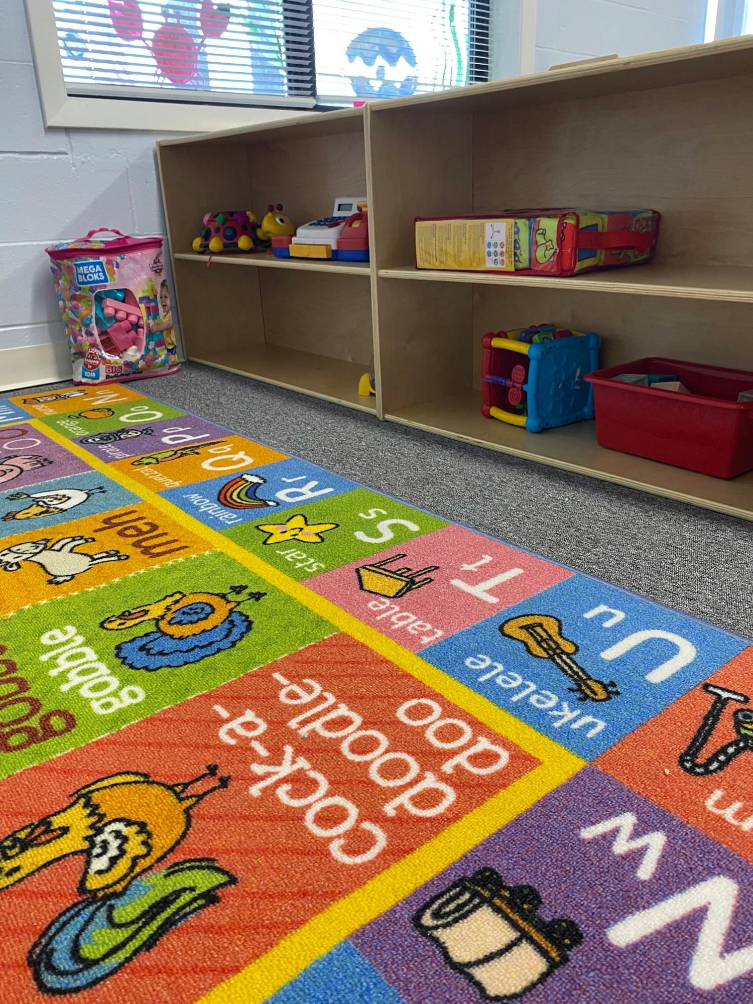 Alphabet rug on floor with shelves of toys in a classroom