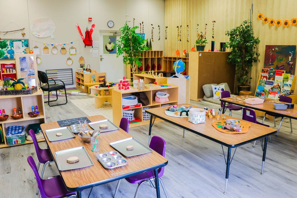 Classroom with tables and chairs, shelves with toys and books