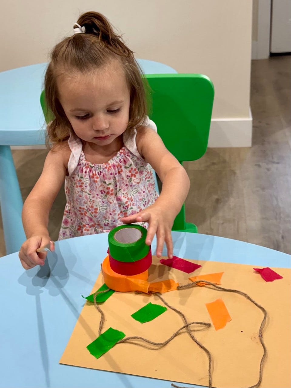 Child at a table making a craft with tape and string