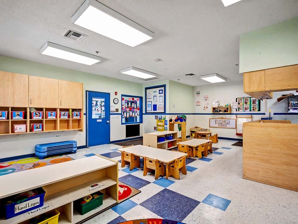 Empty classroom with small tables and chairs, storage cubbies, and blue door