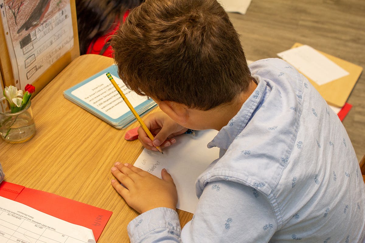 Child writing on paper with a pencil at a desk