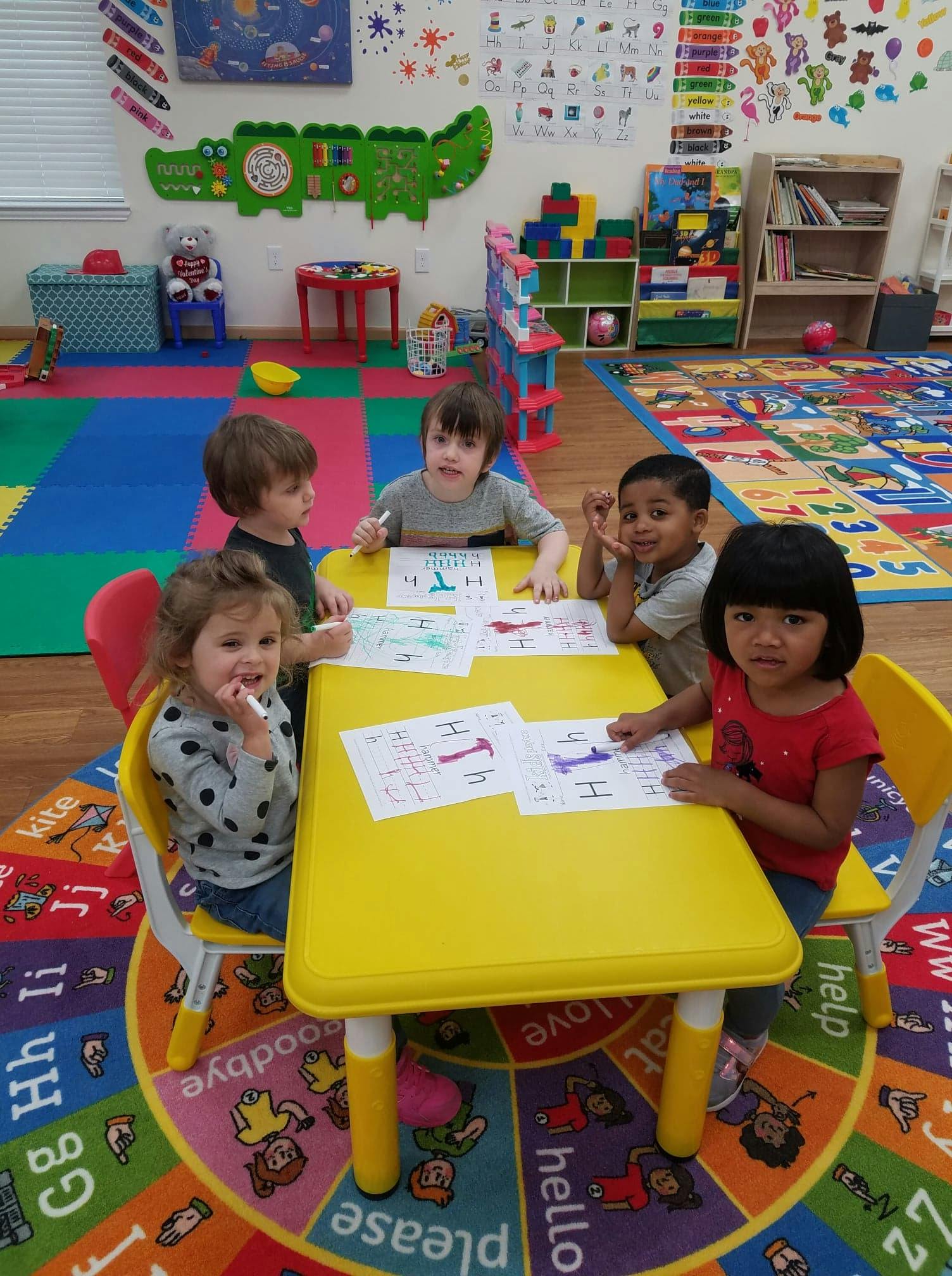 Children sitting at a table drawing in a classroom, drawing on papers