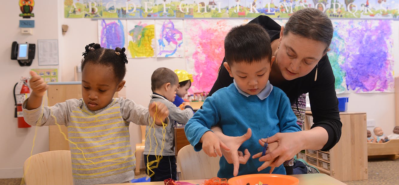 Adult and two children interacting with objects at a table in a classroom