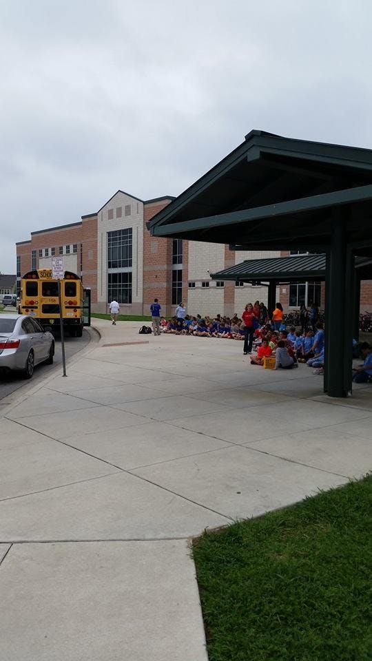 School building with a bus and people sitting on the ground outside