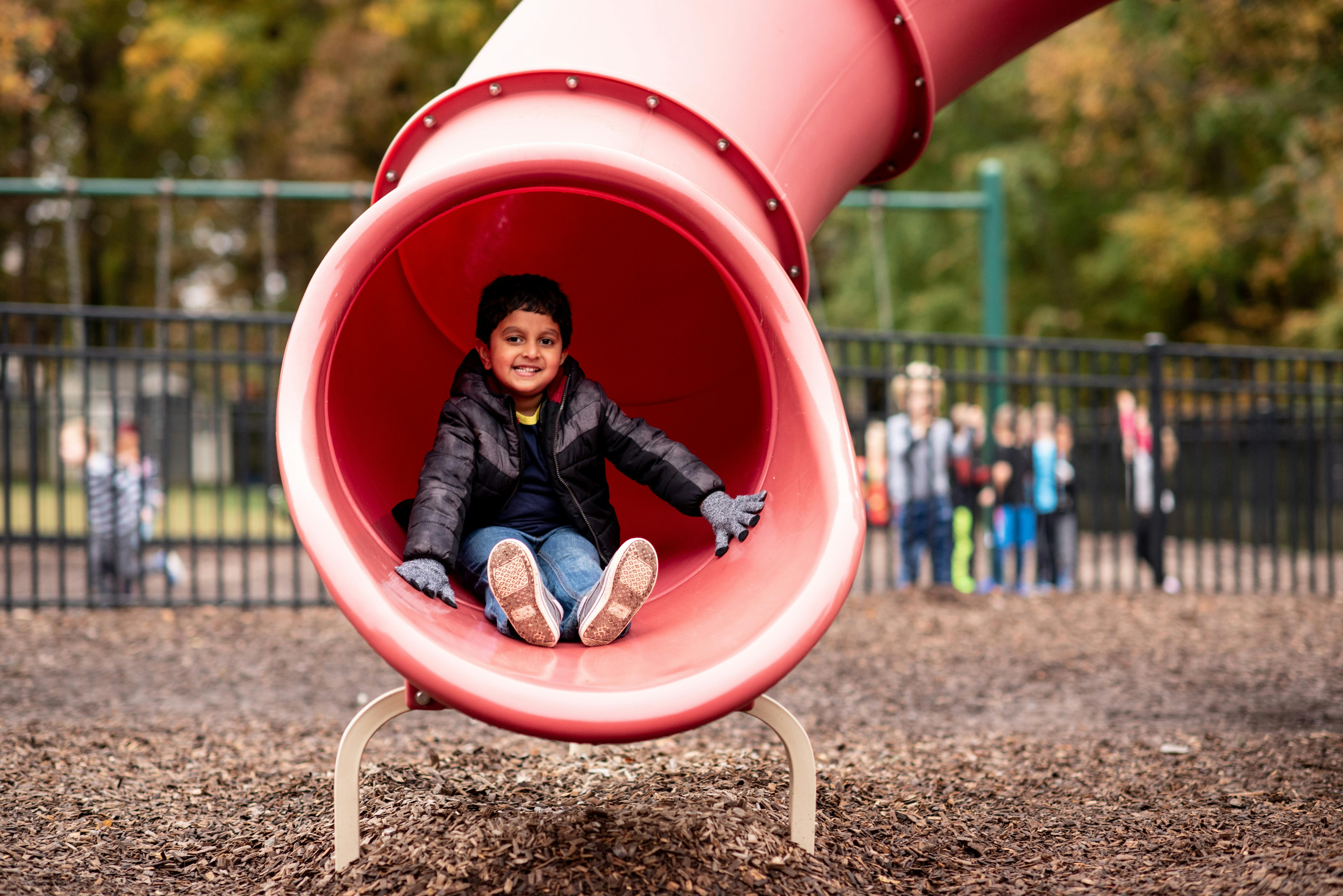Child sitting at the bottom of a red playground slide