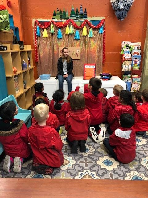 Person sitting on a stage in front of children in a group of children