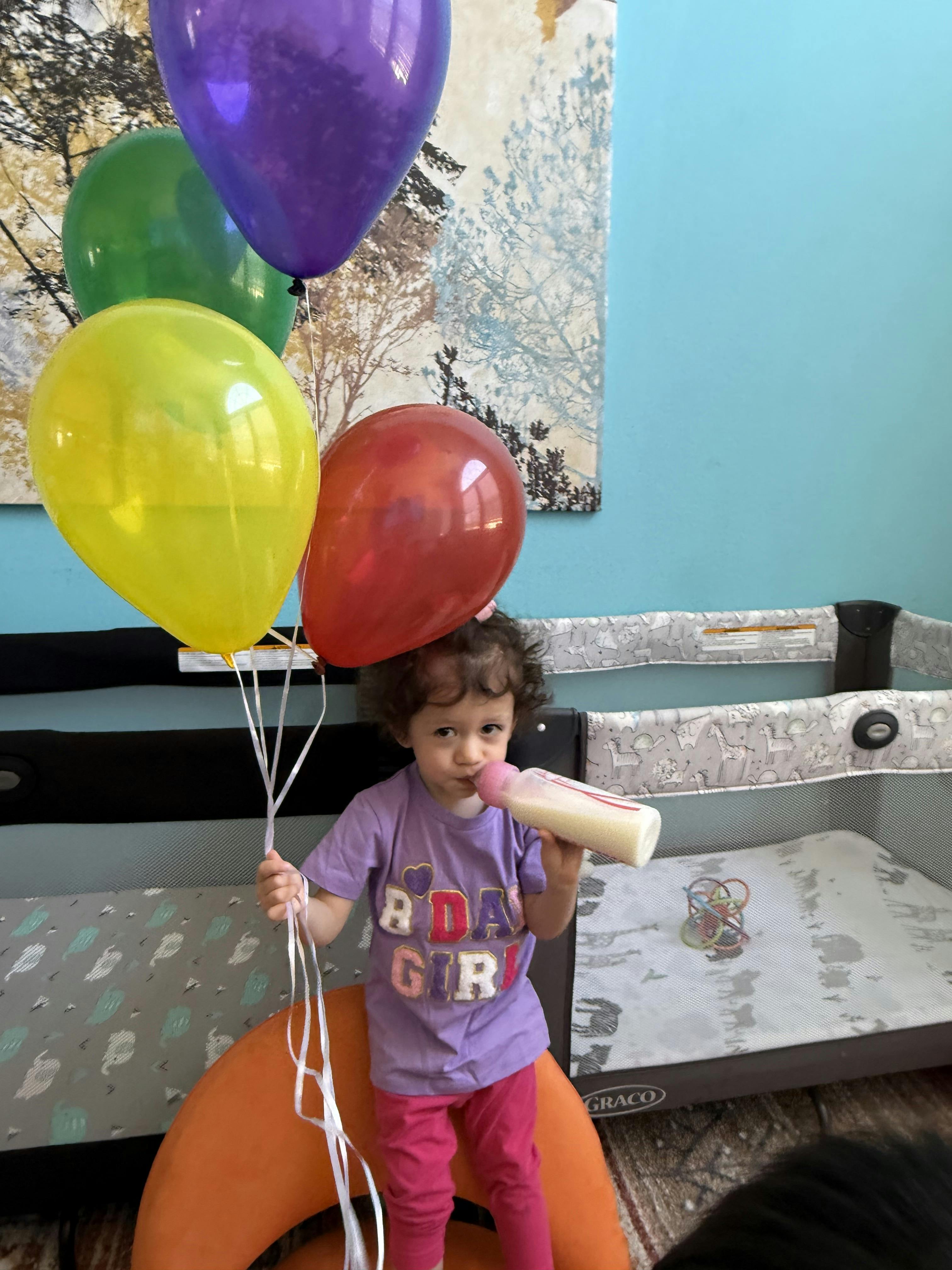 Child holding balloons and drinking from a bottle