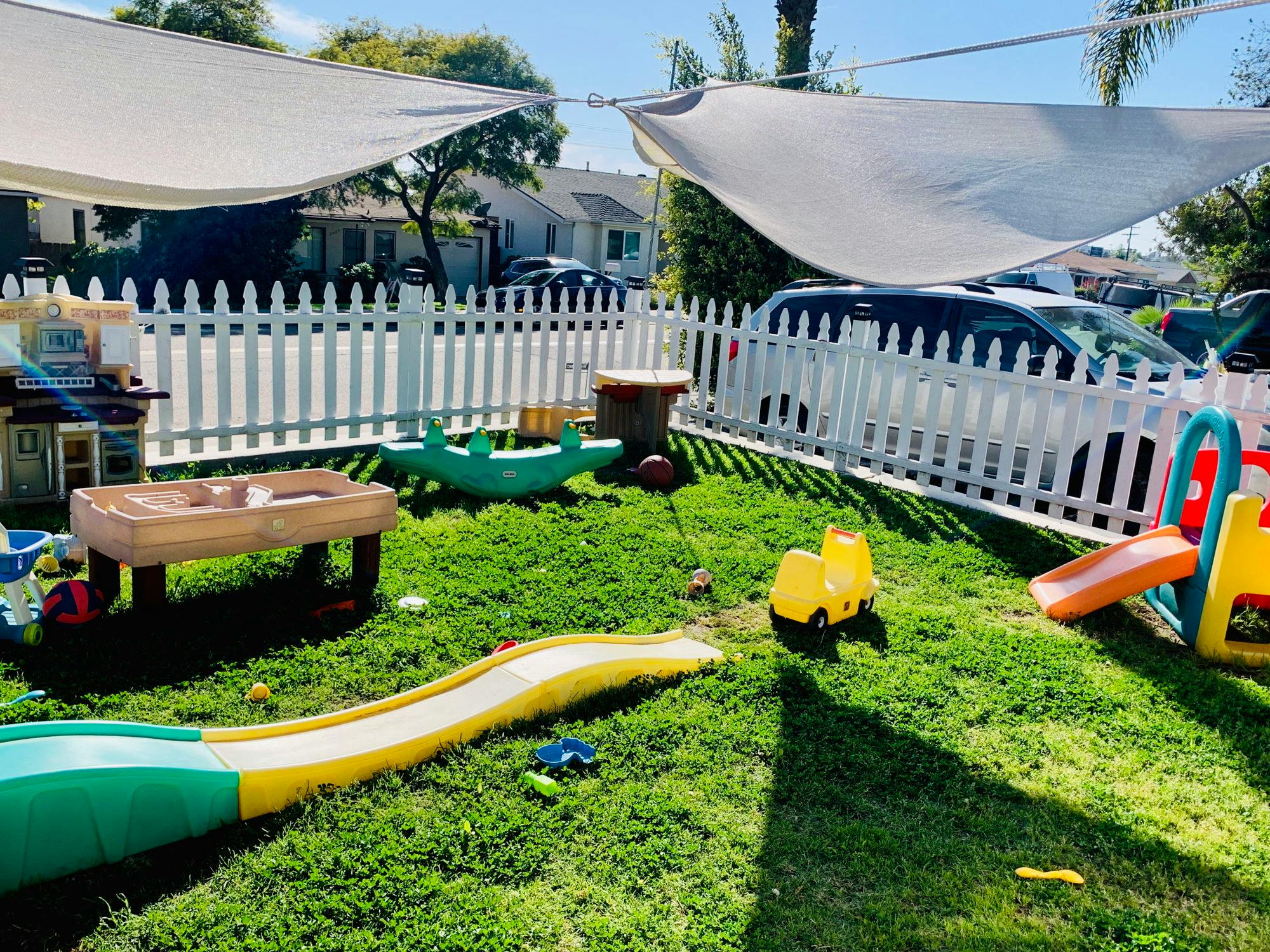 Outdoor play area with slides, toys, and a white picket fence