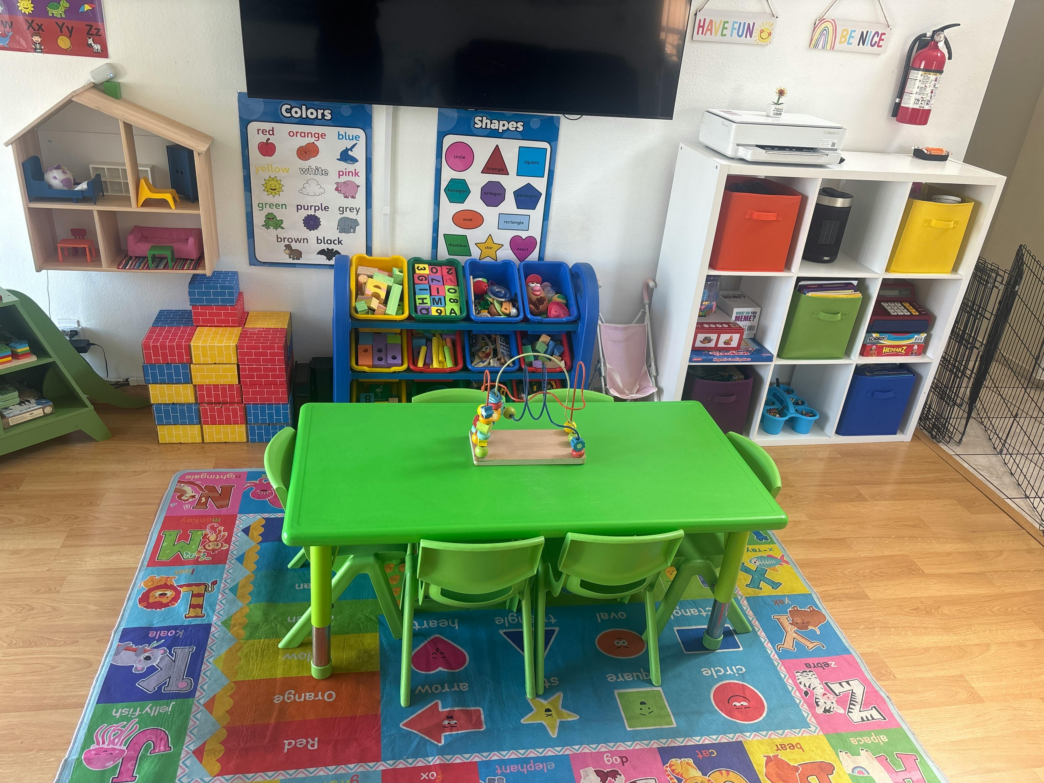 A children's play area with a green table and chairs, storage for toys, and educational posters