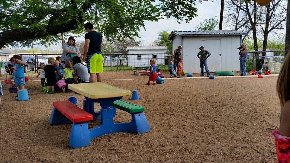People and children on a dirt playground with a small picnic table