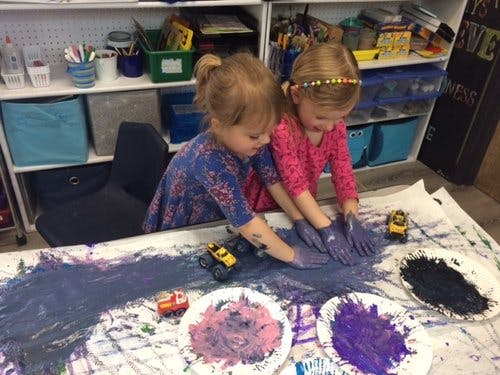 Two children finger painting with purple and black paint