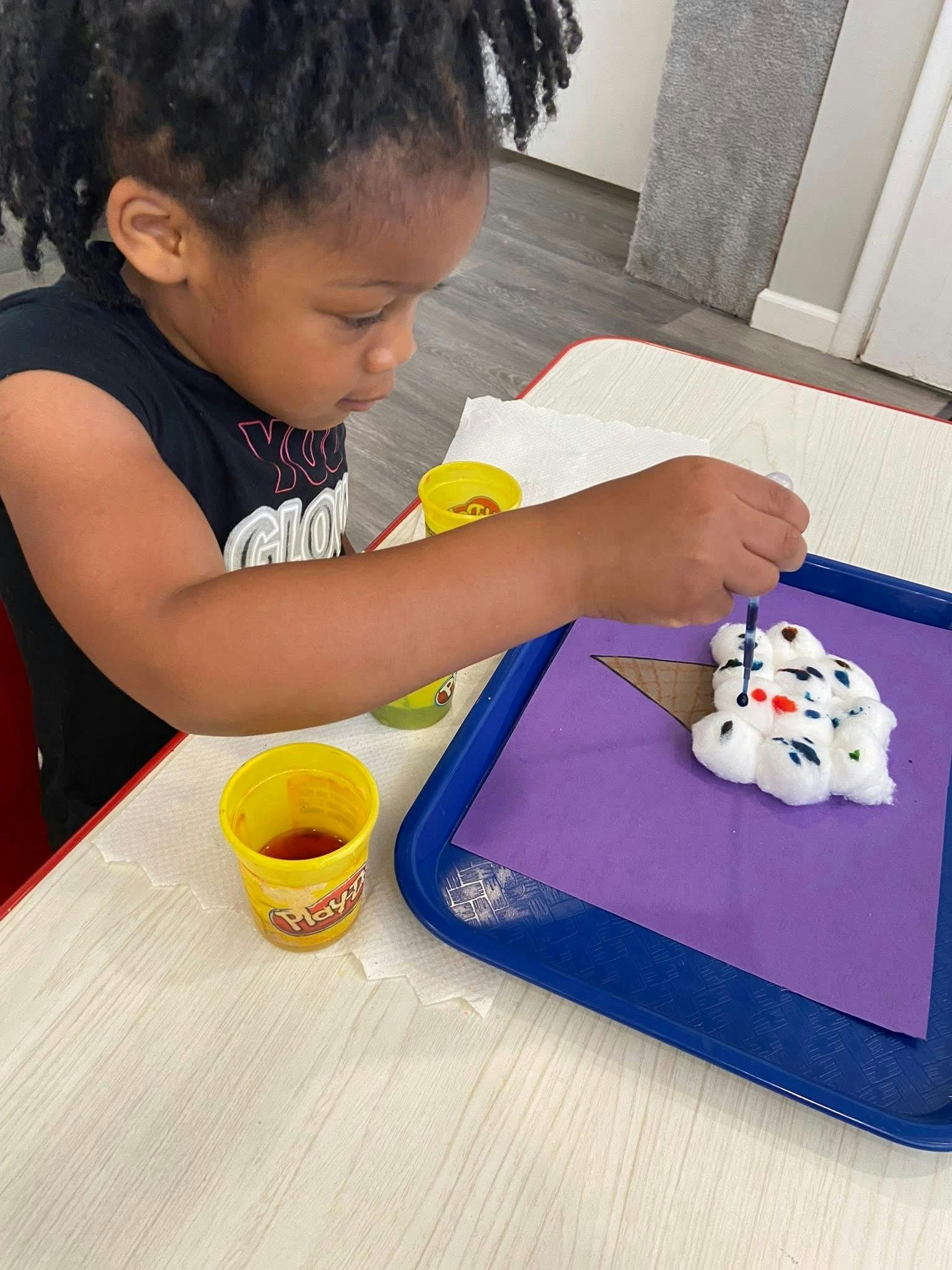 Child using a dropper to add liquid to cotton balls on a paper craft