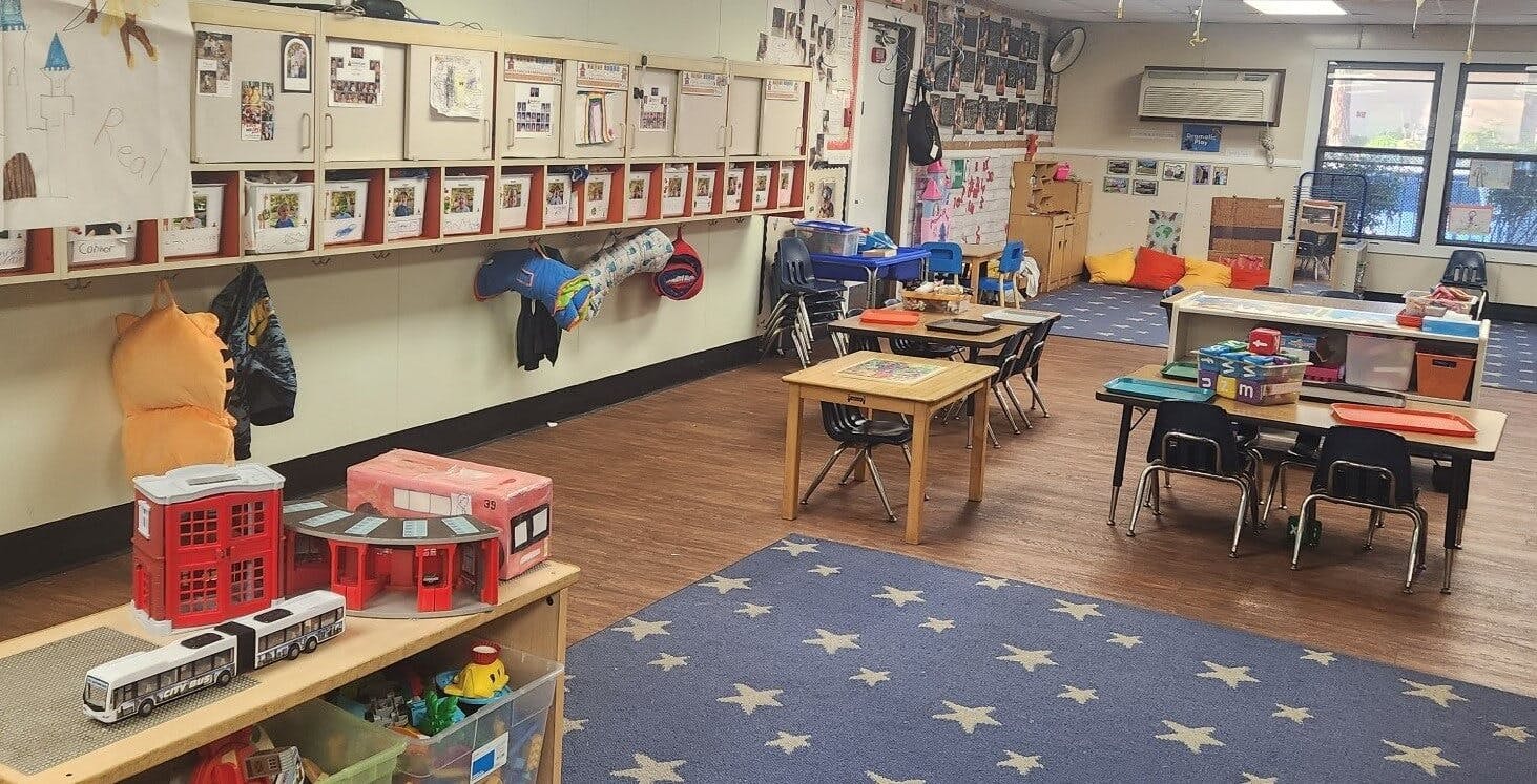Classroom with child-sized tables and chairs, cubbies, and play areas