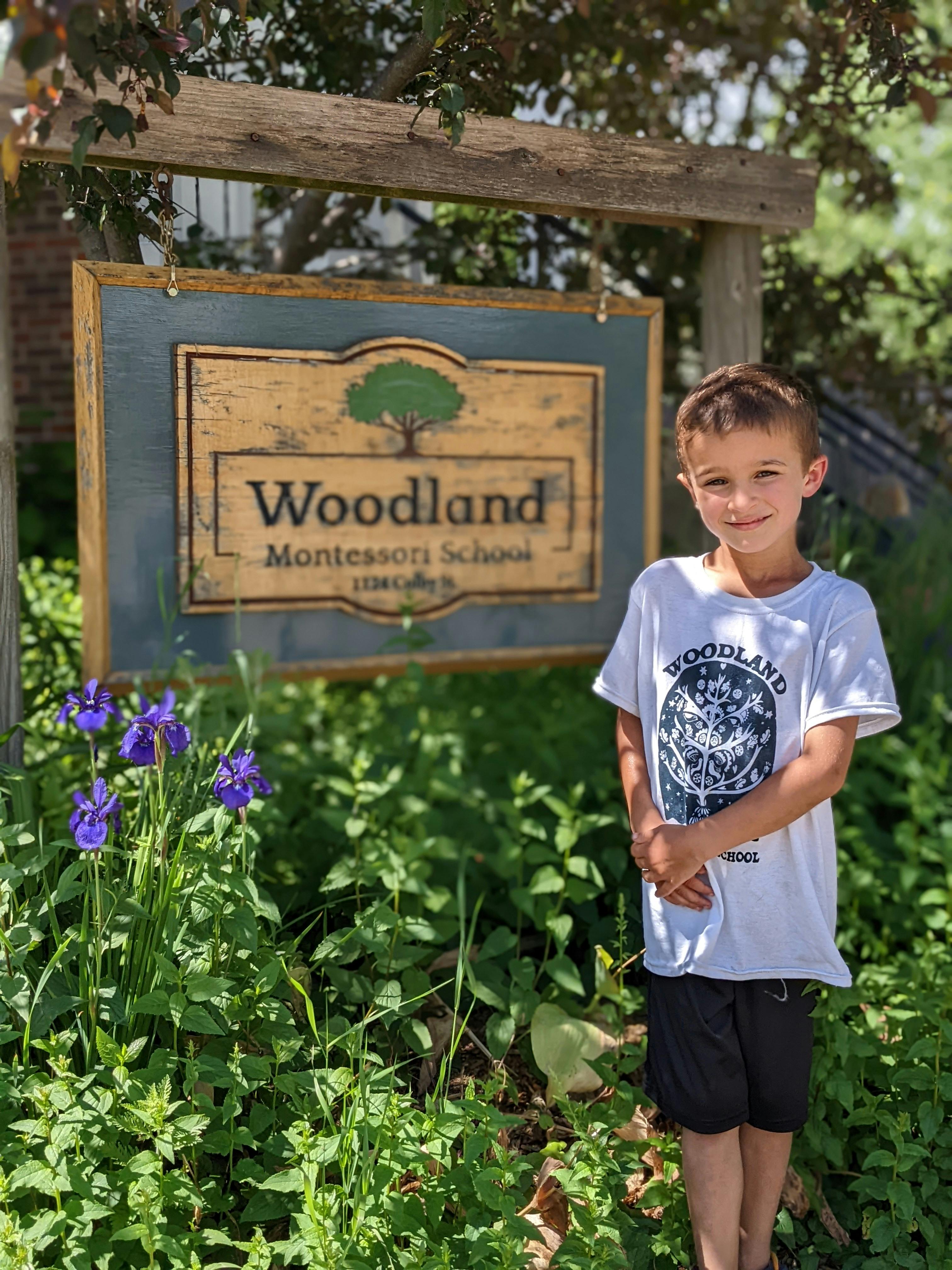 Child standing in front of a sign for Woodland Montessori School