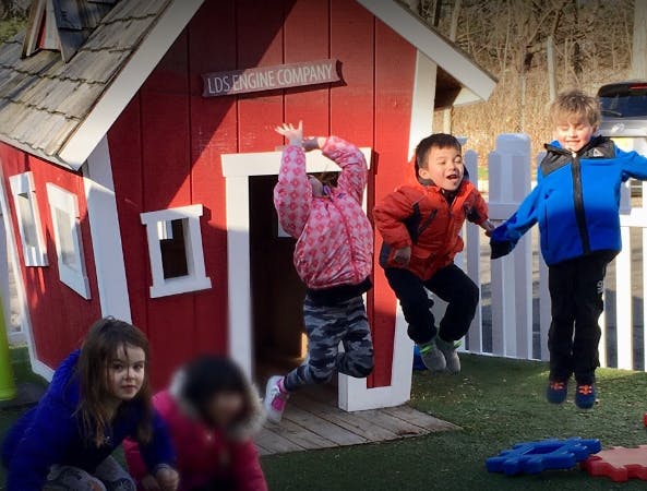 Children jumping in front of a red playhouse