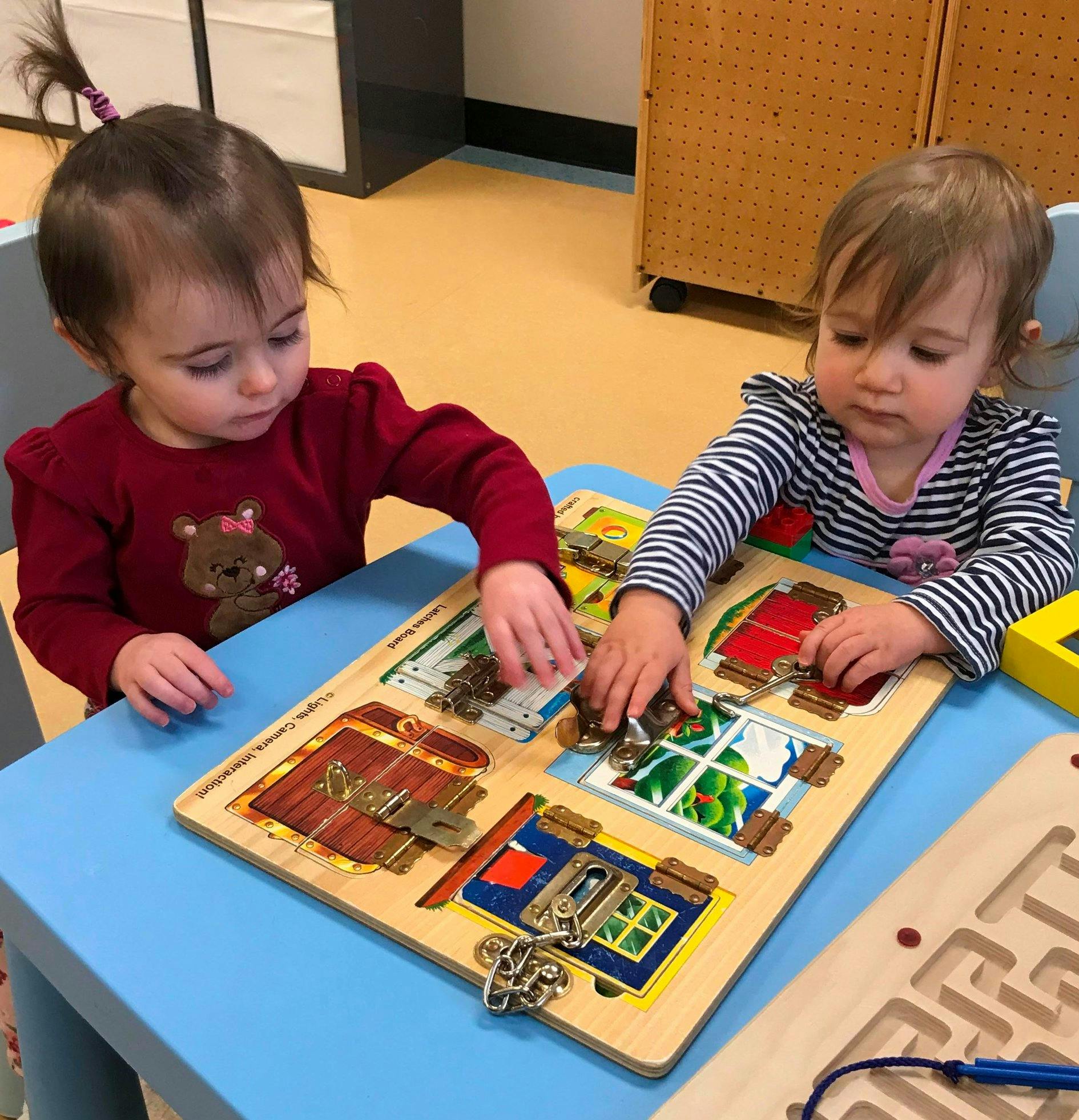 Two children playing with a wooden latch board on a blue table