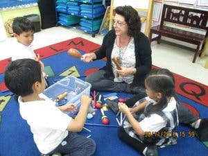 Adult and three children playing with musical instruments in a classroom