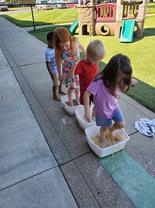 Children stepping through bins of sensory materials outdoors