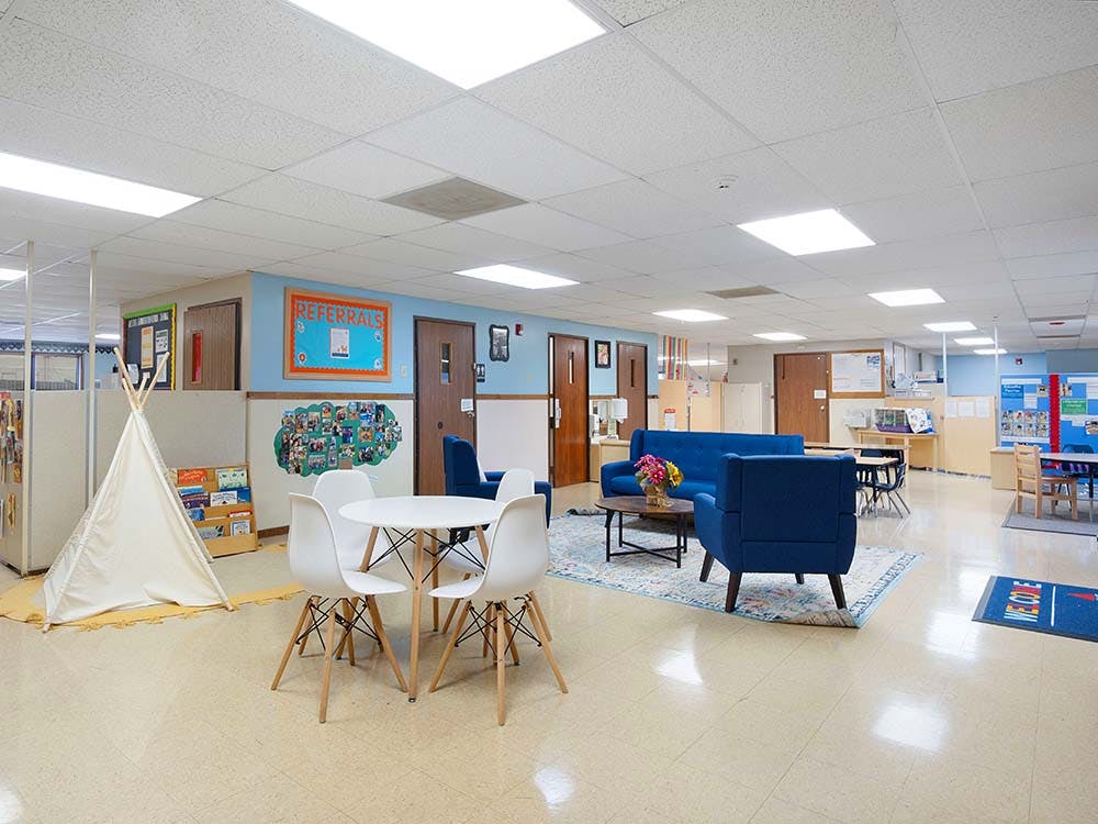 Lounge area in a classroom with blue couches, white chairs, and a teepee