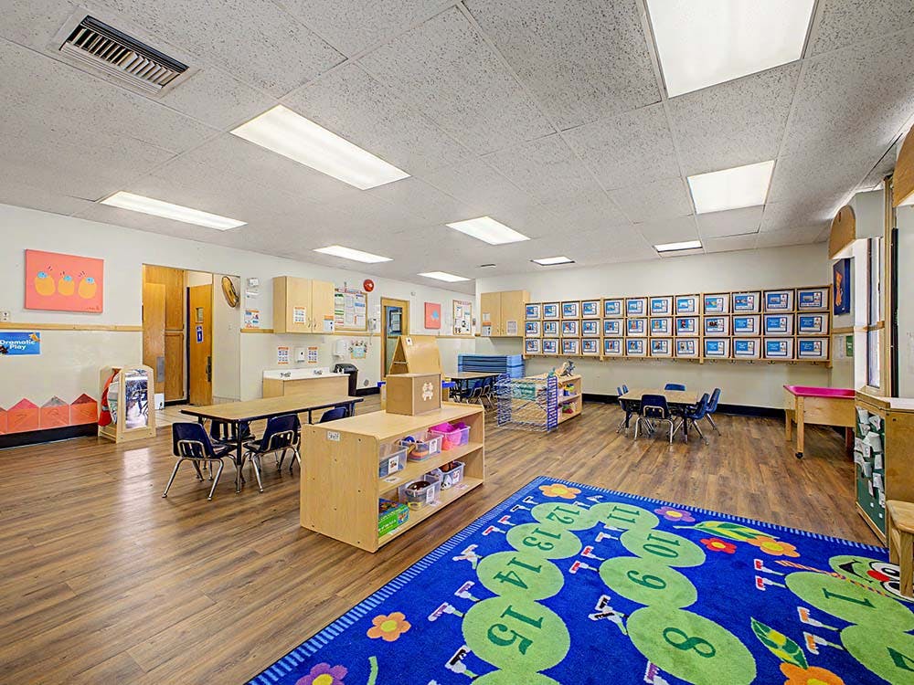 Classroom with child-sized tables and chairs and a colorful number rug