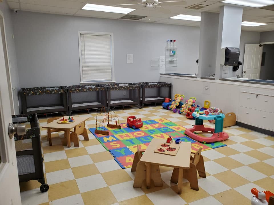Daycare room with cribs, playmats, and small tables