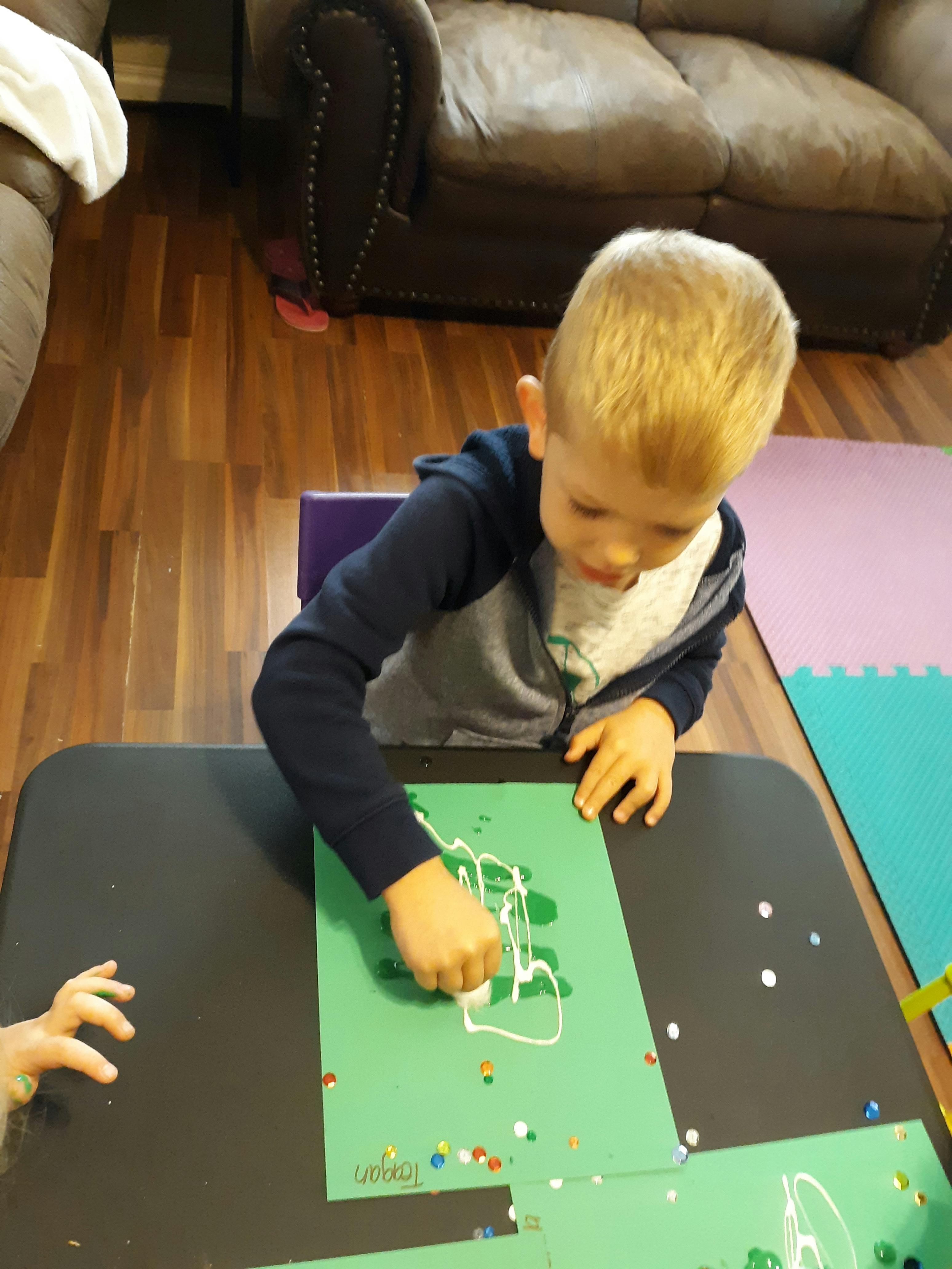 Child drawing on green paper with white glue