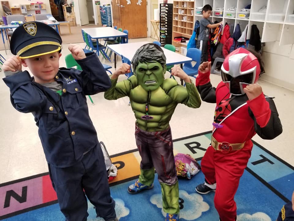 Three children in costumes flexing in a classroom