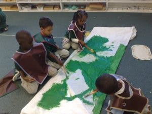Children painting on a large white canvas on the floor
