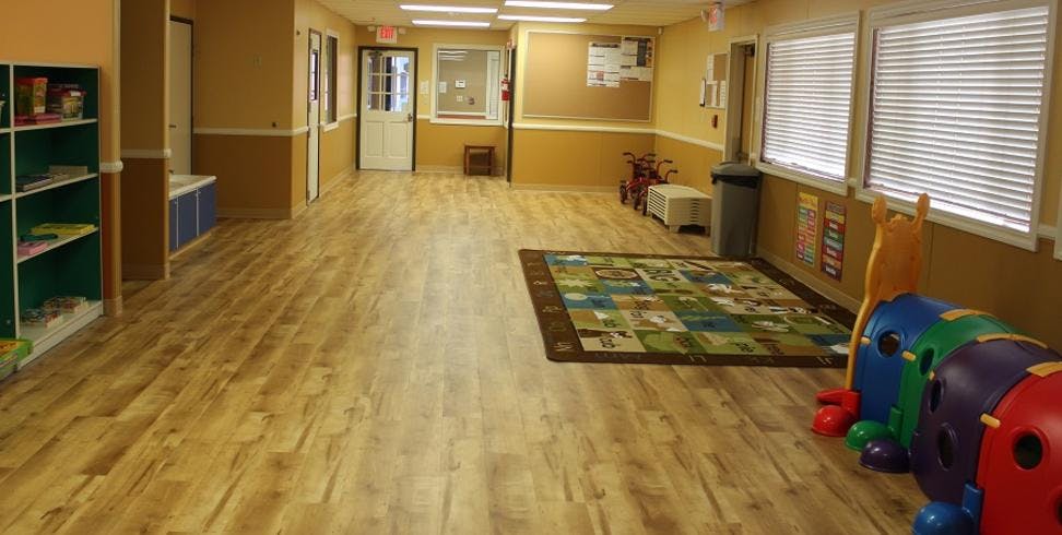 Empty classroom with wooden floor, colorful rug, and children's toys