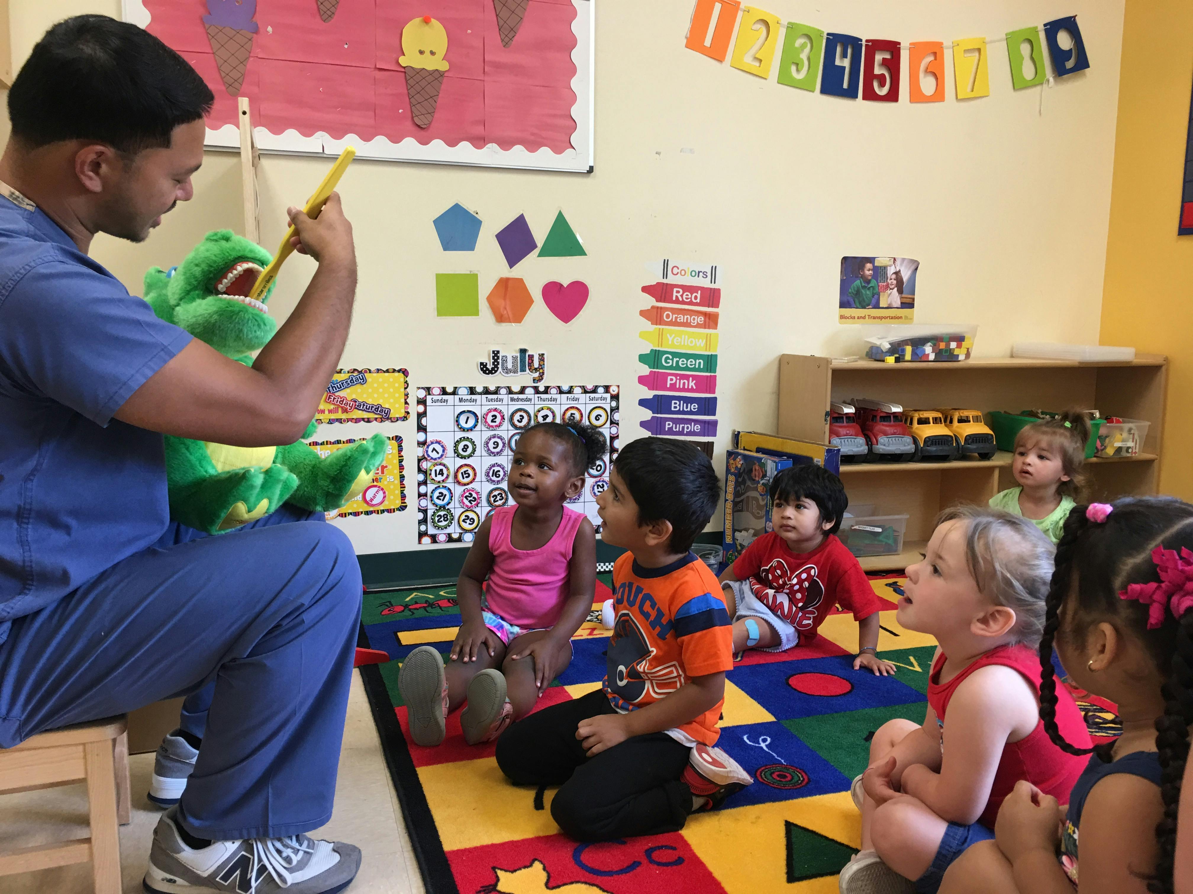 Person holding a puppet for children sitting on a rug in a classroom