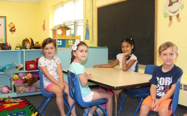 Four children sitting at a table in a classroom