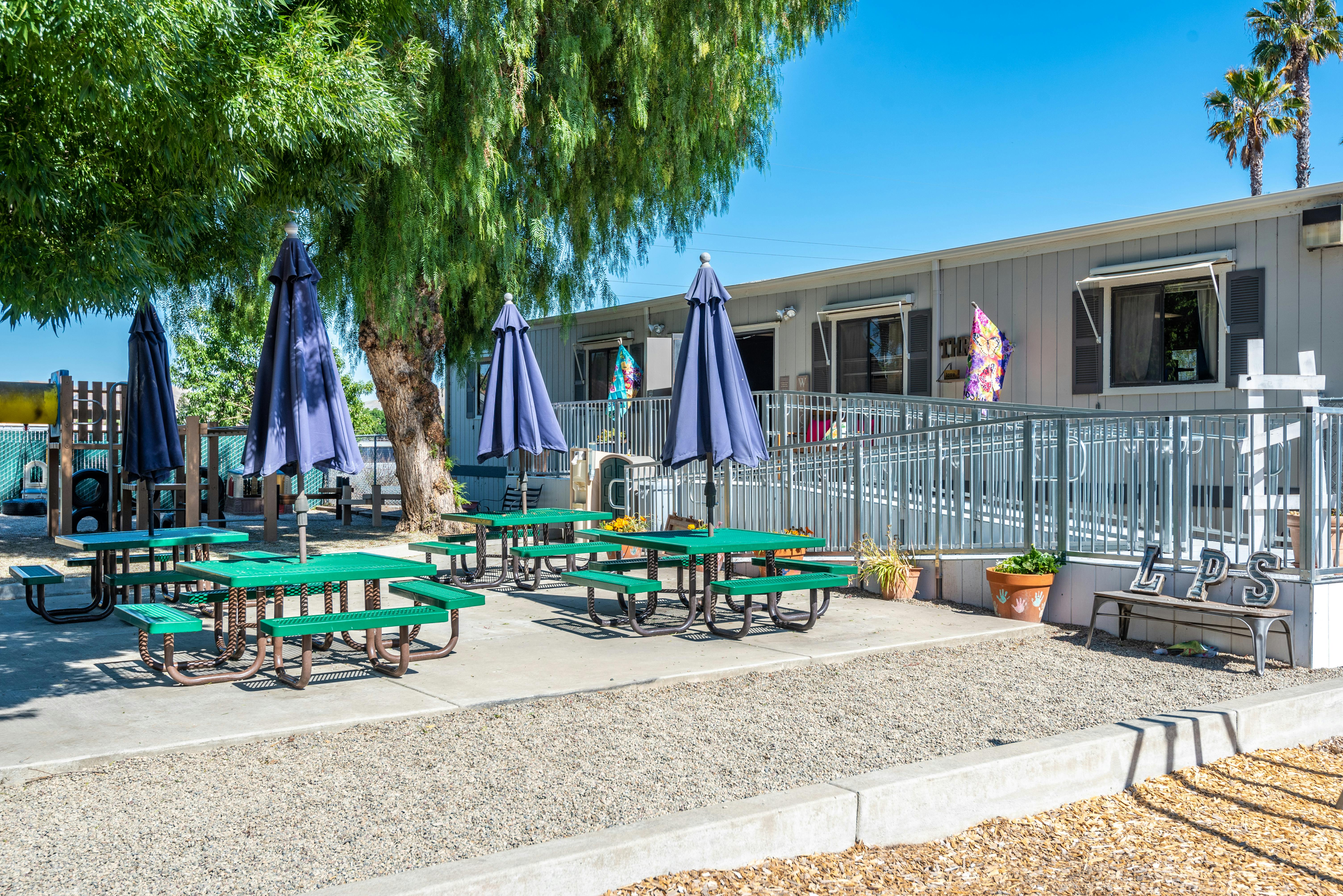 Outdoor eating area with green picnic tables and blue umbrellas