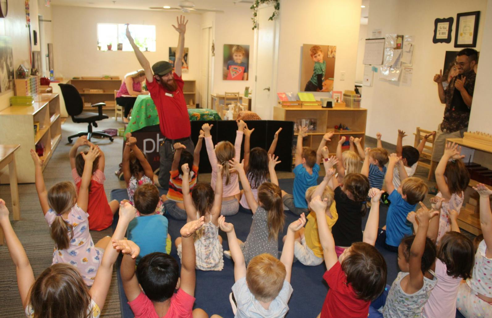Adult and children sitting on floor with arms raised in a classroom