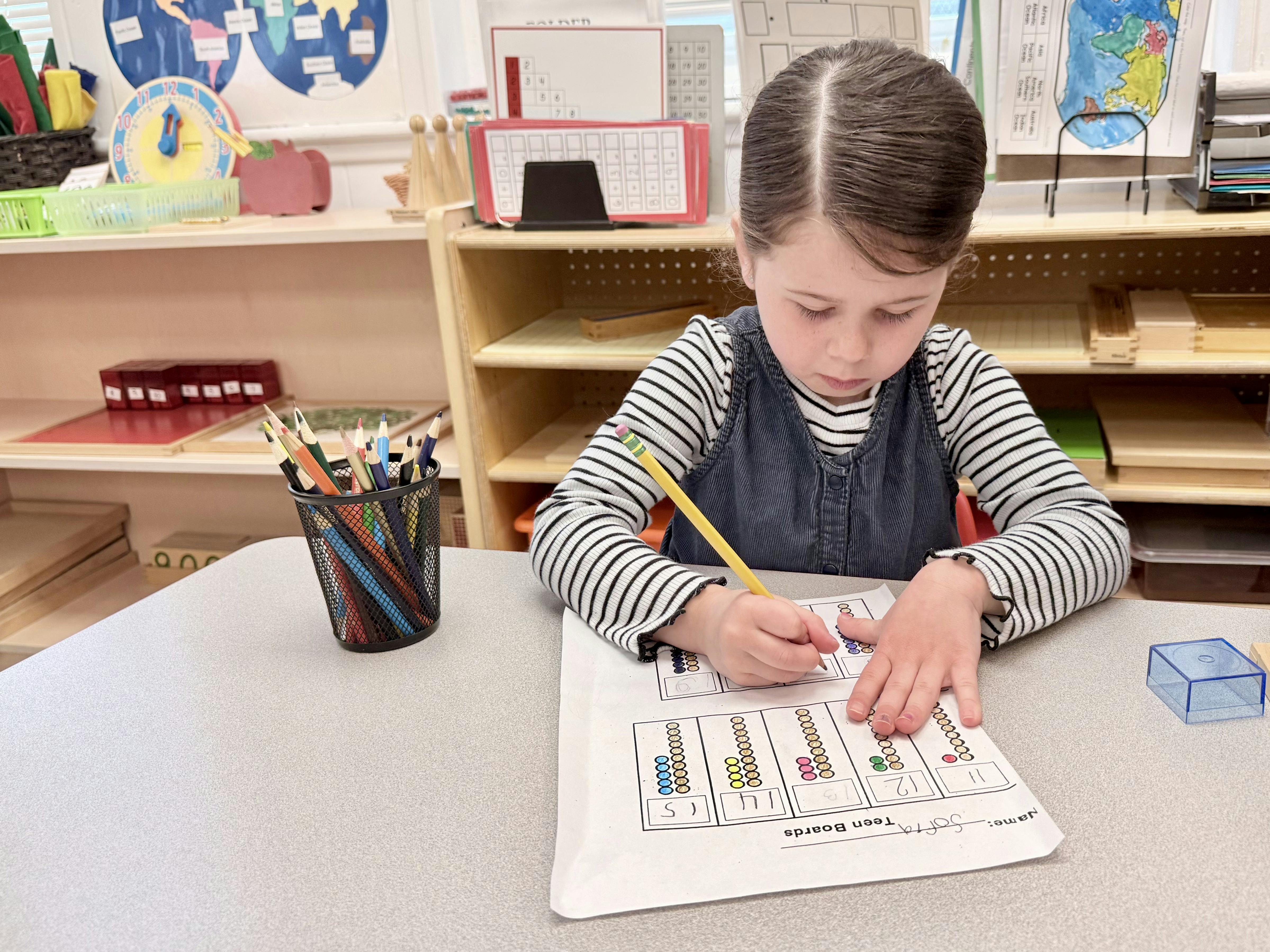 Child writing on a worksheet with a pencil in a classroom