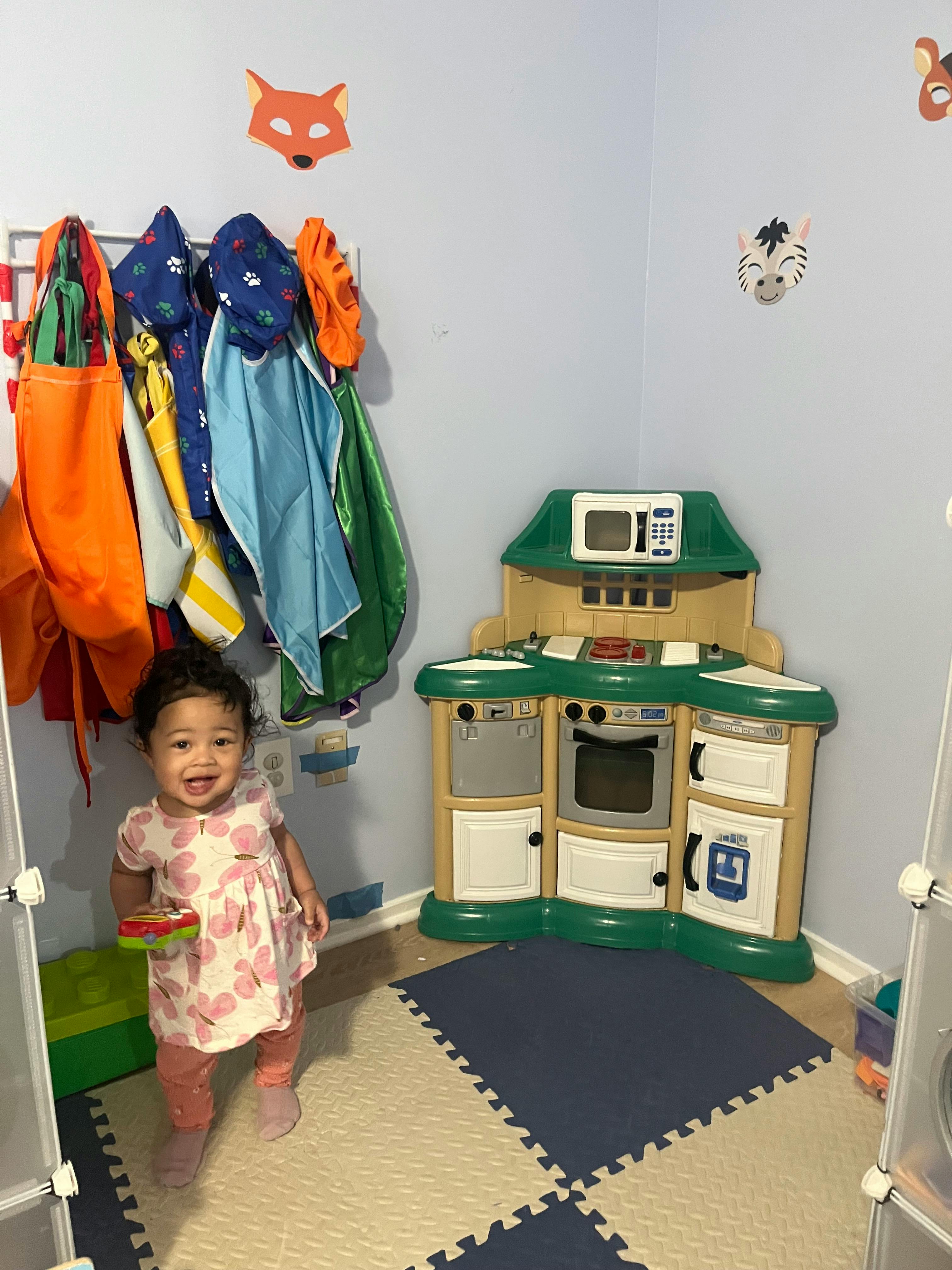 Child smiling at the camera next to a toy kitchen and play mats