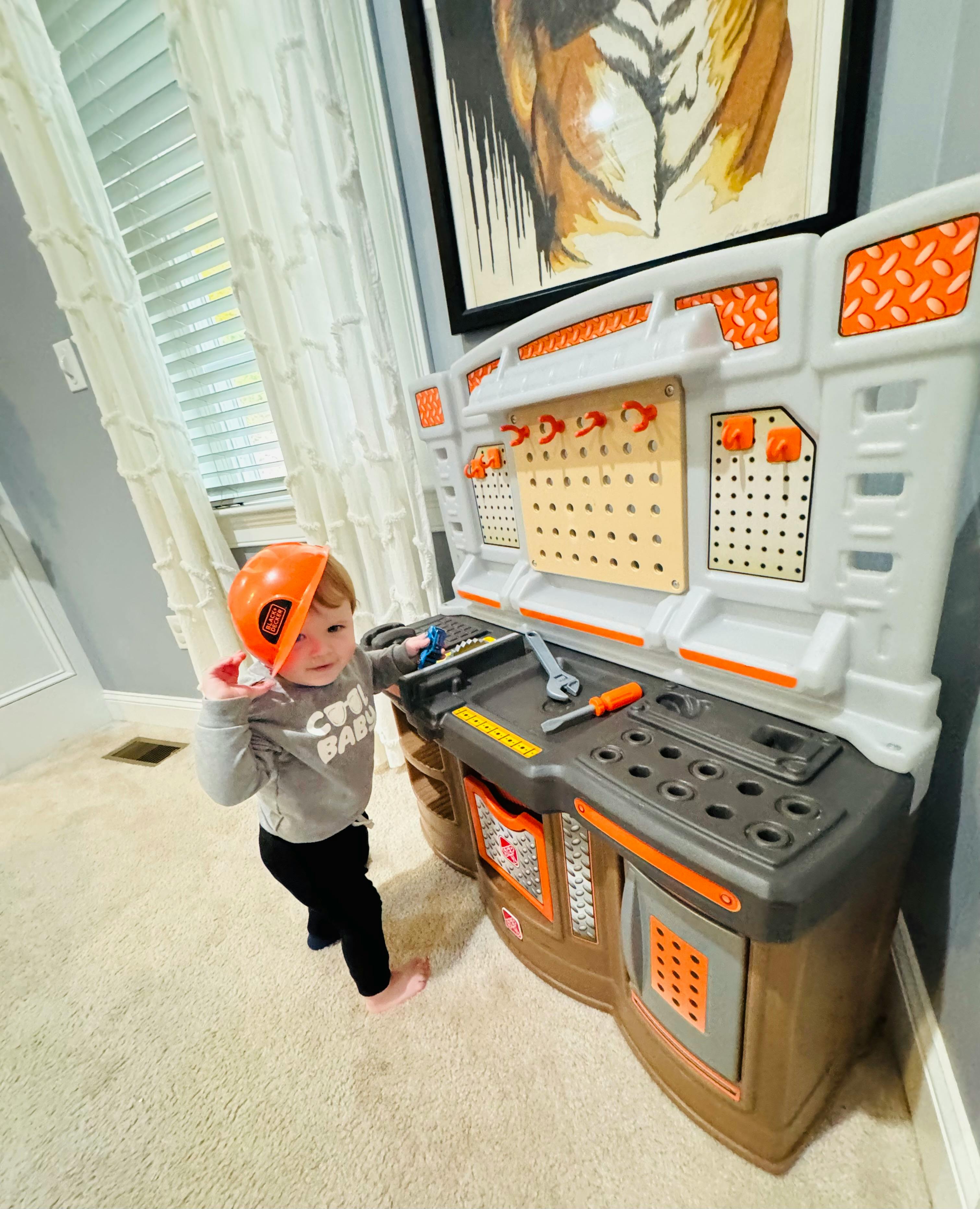 Child wearing an orange hard hat playing with a toy workbench