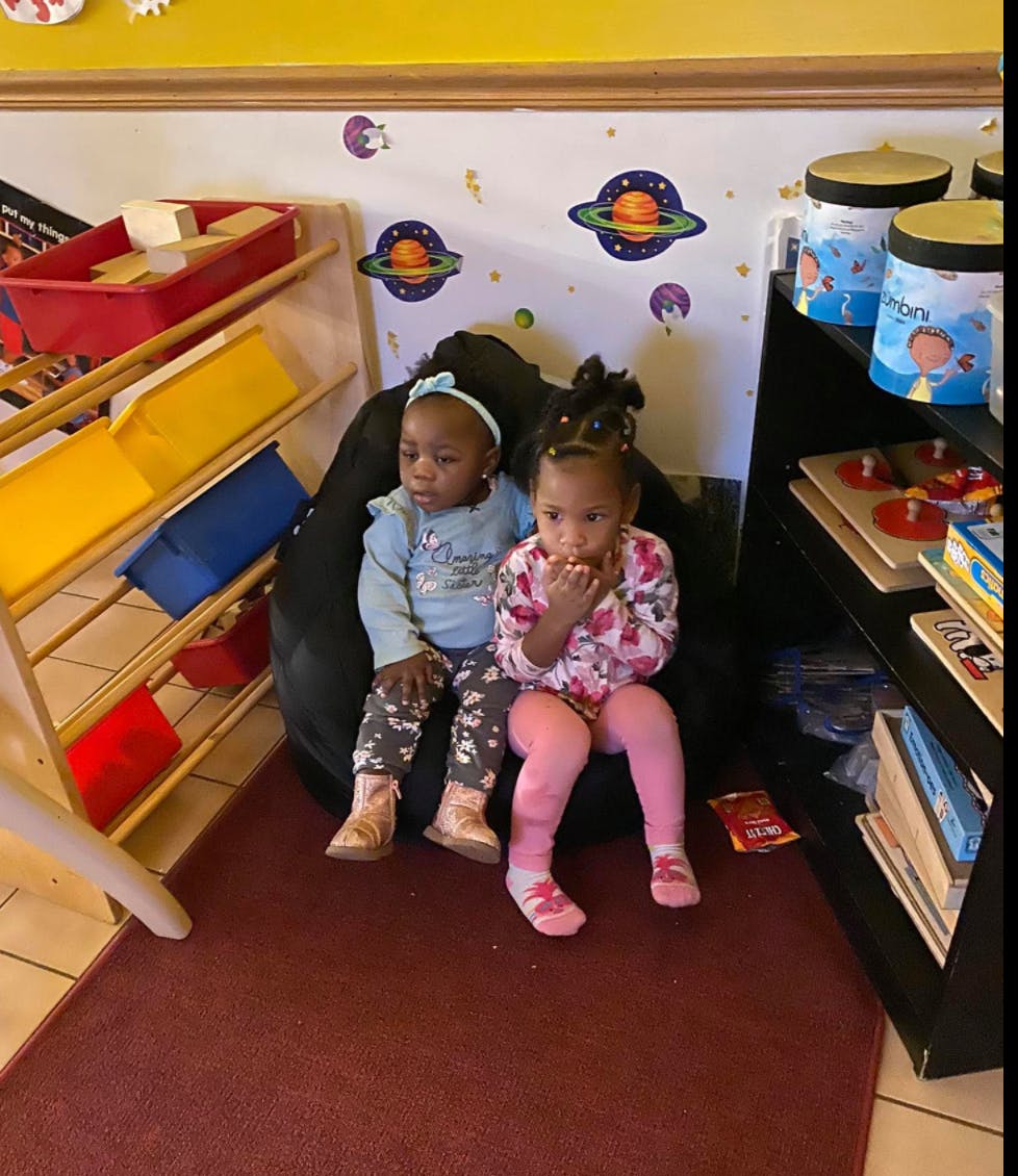 Two children sitting on a beanbag chair in a room with space-themed wall decals
