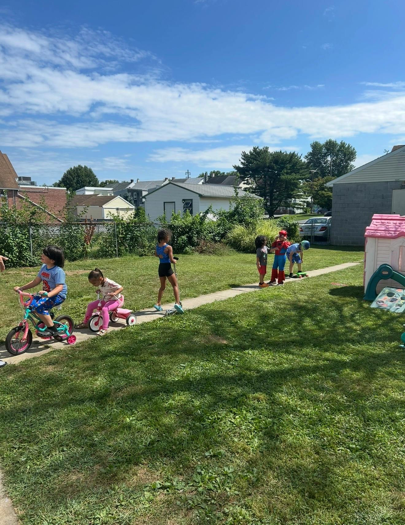Children playing with bikes and scooters on a sidewalk in a yard