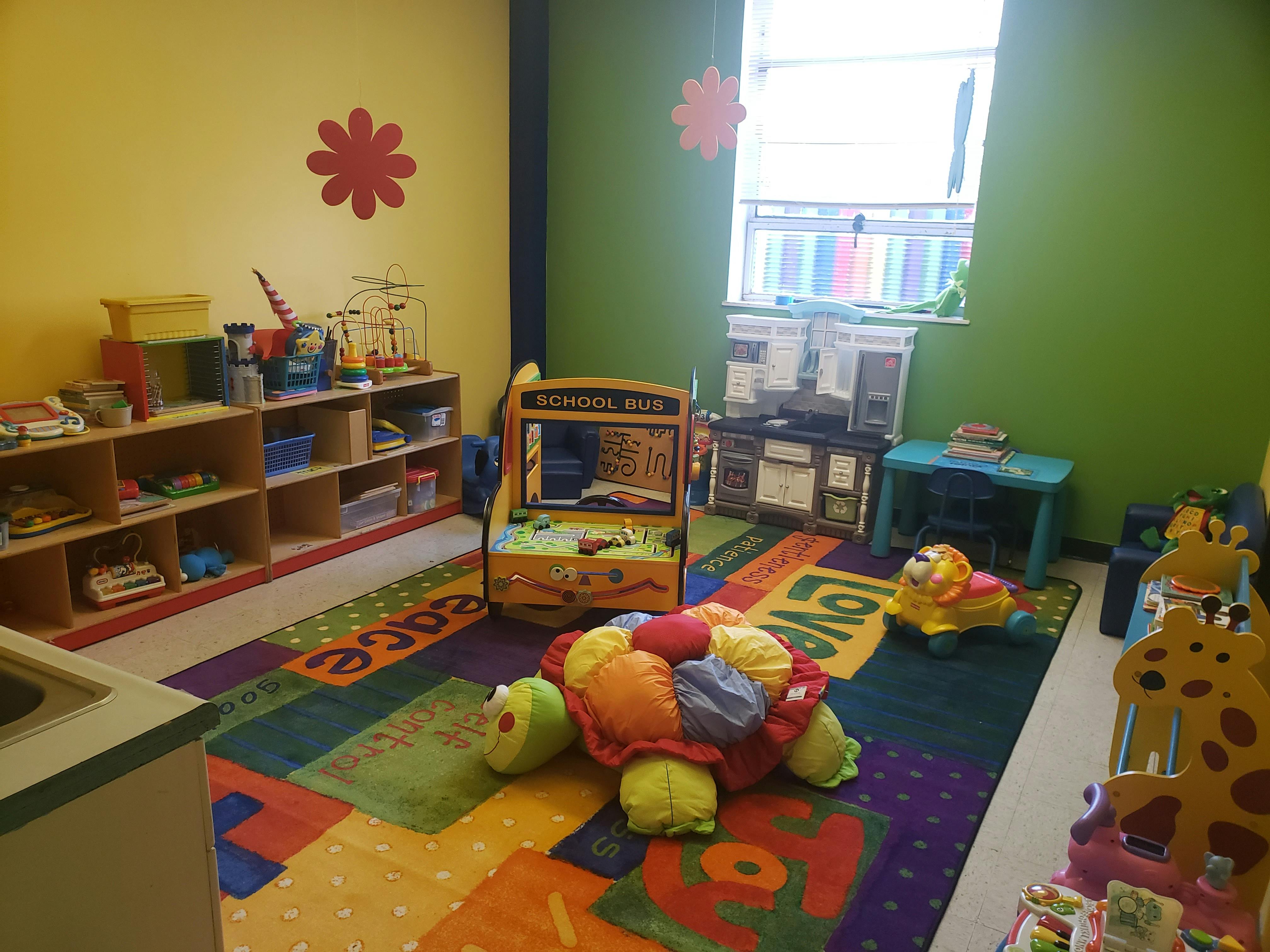 Playroom with colorful rug, shelves of toys, and a toy school bus