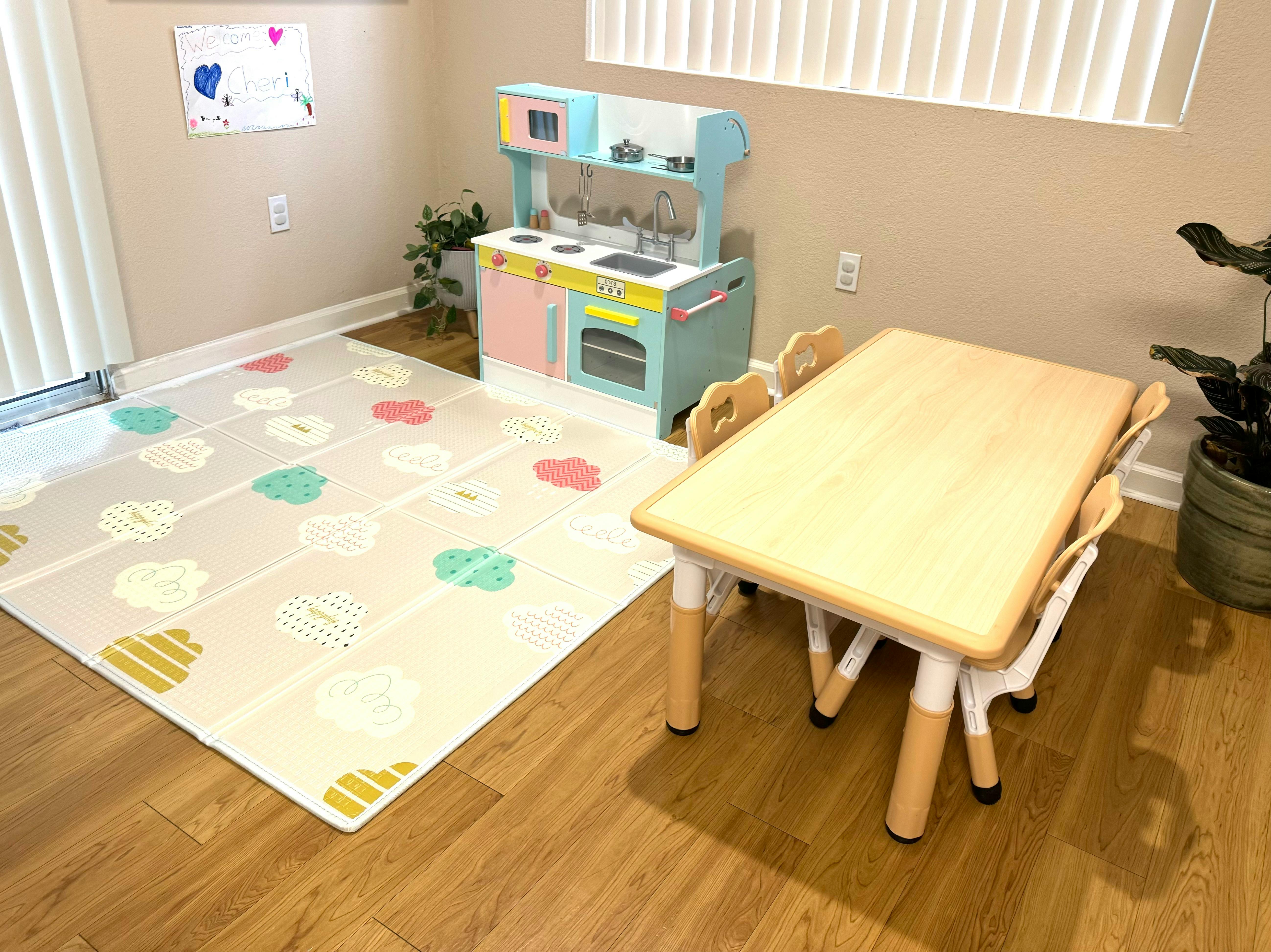 Children's play kitchen, rug, and table with chairs in a room