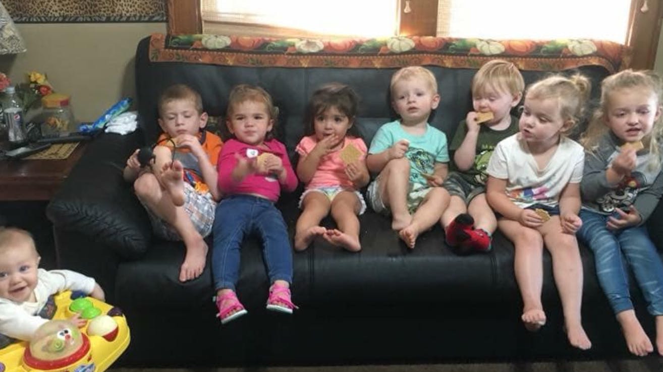 Multiple children sitting on a couch, some holding food