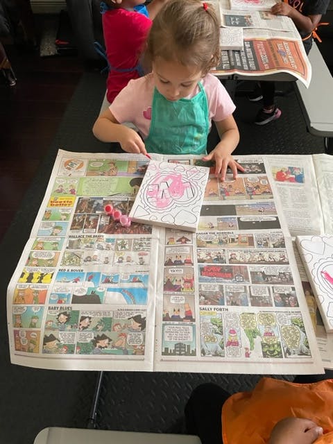 Child coloring a picture on a newspaper-covered table