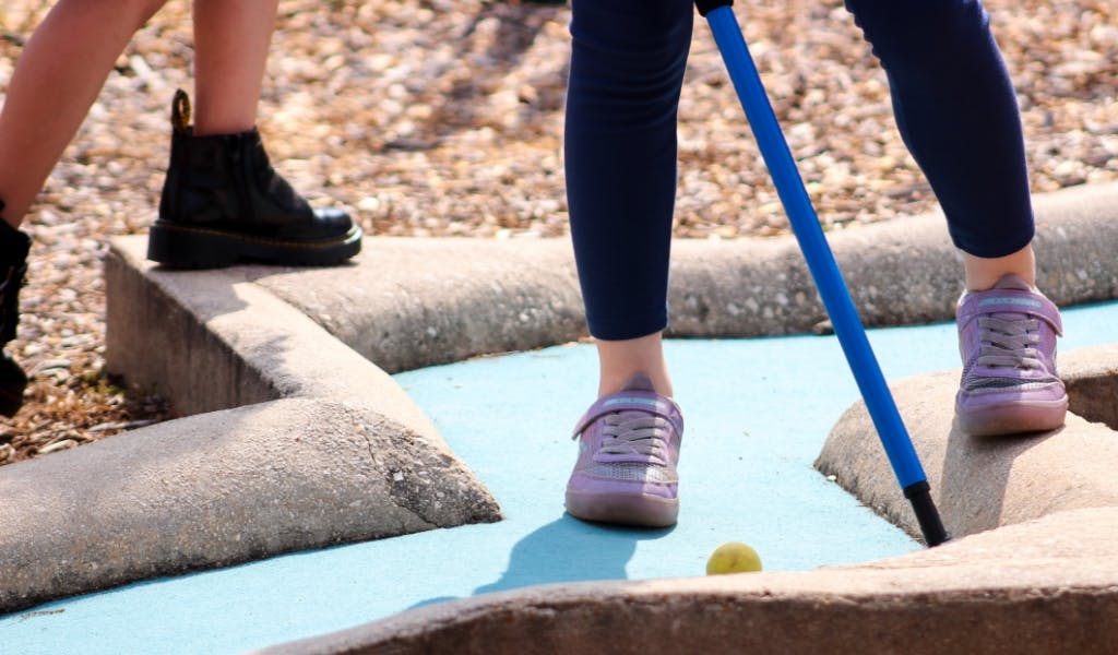 Person playing mini golf with a blue putter and yellow ball